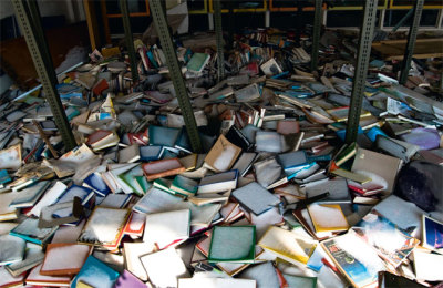 Snow on books that has fallen through the smashed floor to ceiling windows of a now abandoned school library.