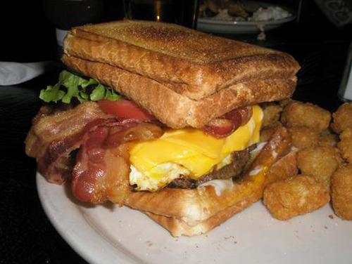Double Bypass Burger A burger topped with five slices of bacon, four slices of cheese, two fried eggs, mayo, lettuce, tomato, and onion between two grilled cheese sandwiches. (Submitted by Kyle Korchran via thevortexbarandgrill)